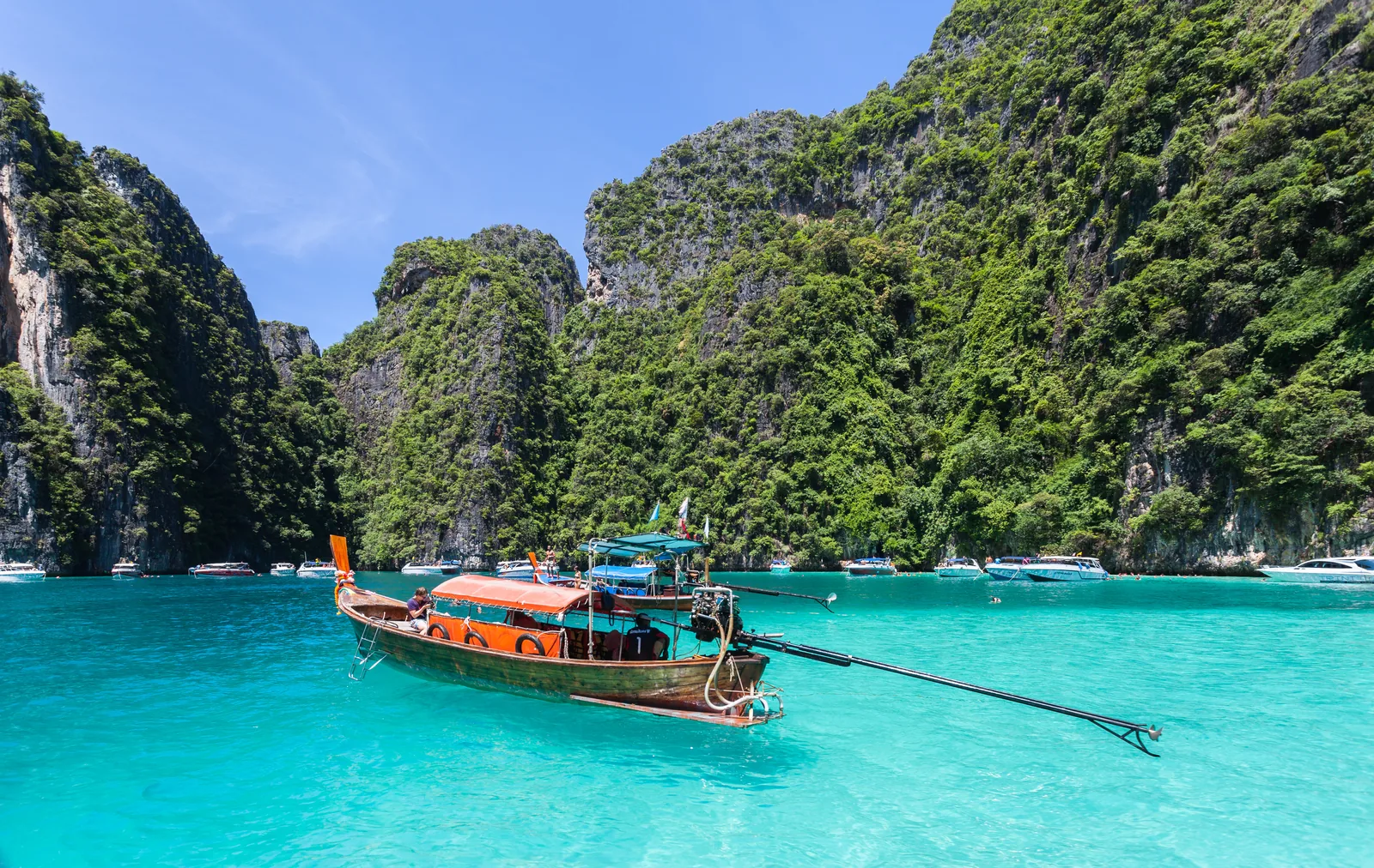 Longtail boat on turquoise water below forested limestone cliffs at Phi Phi Le, Krabi, Thailand